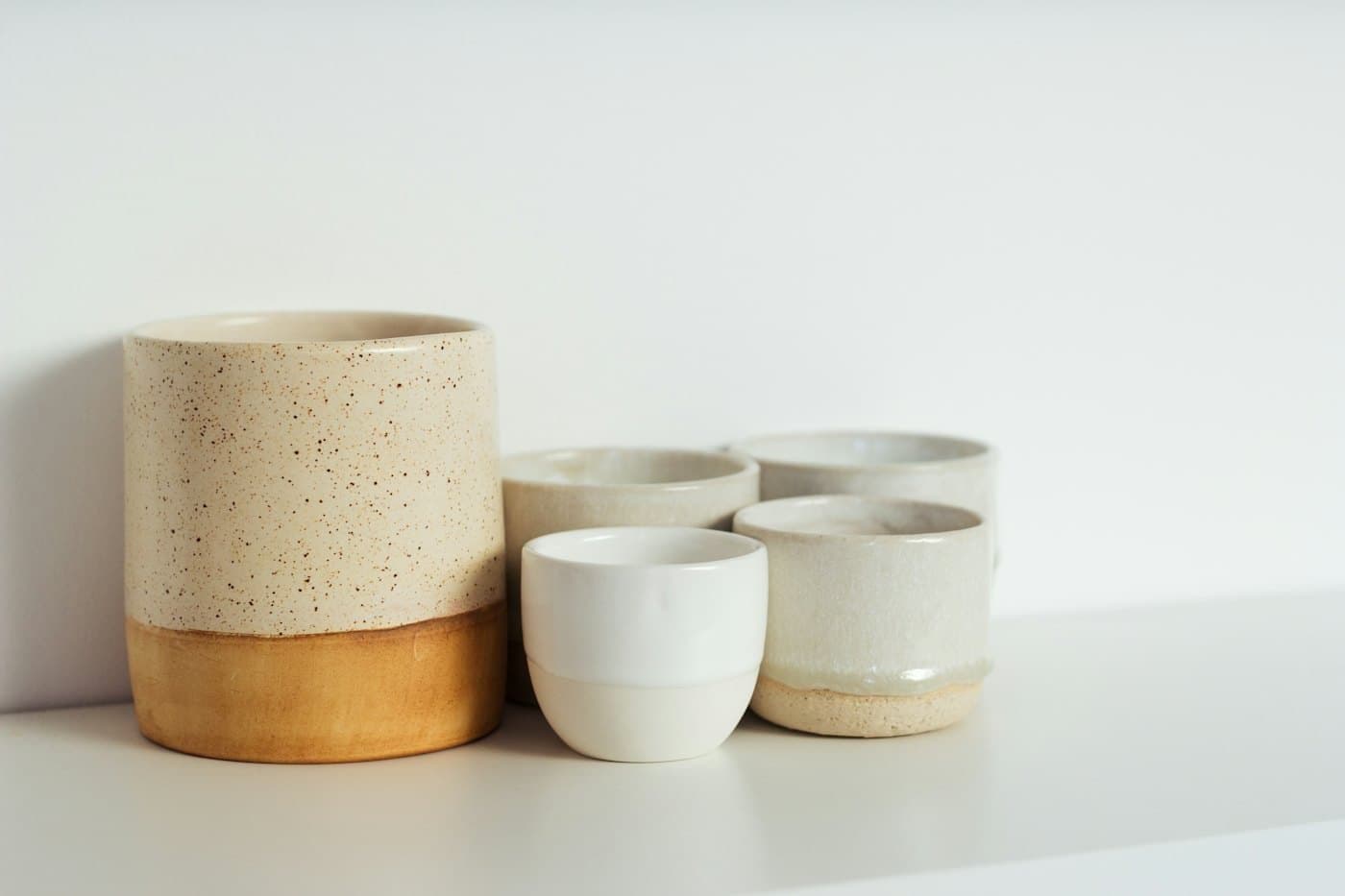 Handmade ceramic cups and a vessel on a white shelf, shown as a study of manufactured goods.
